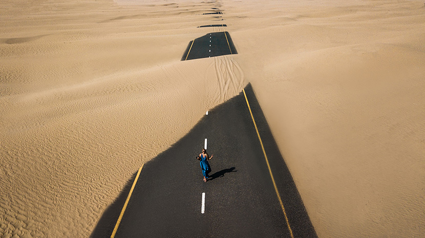 被沙漠覆盖的公路上穿蓝色晚礼服的女人