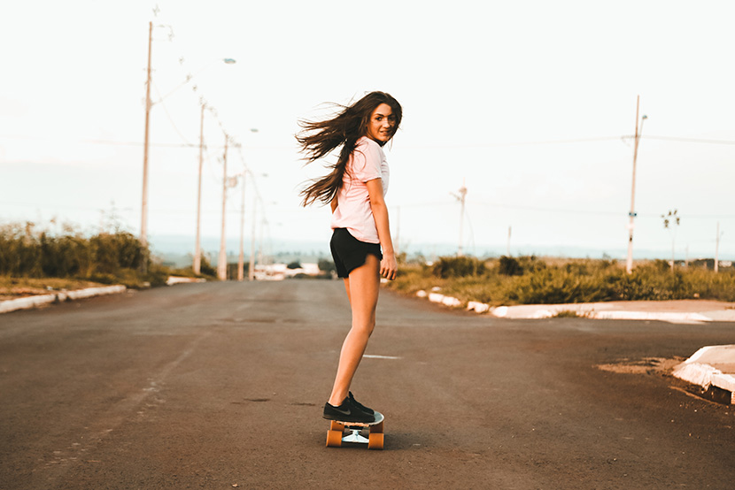 在马路上玩滑板的长发苗条美少女