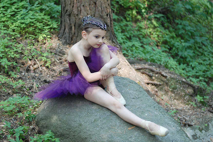 穿紫色芭蕾衣服的小美女坐在大石头上
