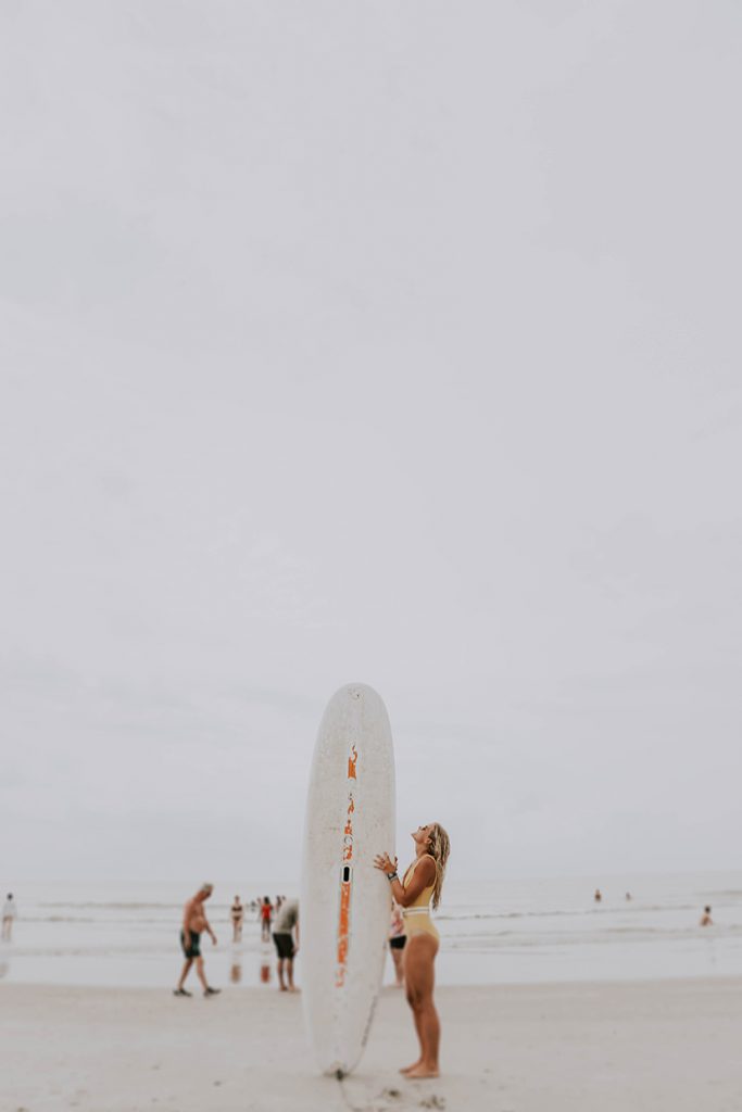 在海边沙滩上拿着冲浪板的妇人