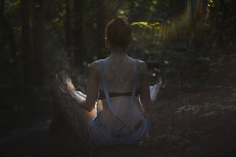 坐在森林晨曦中打坐冥想的性感女人