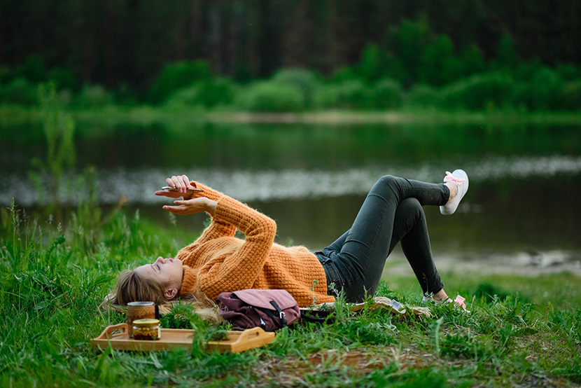 躺在湖边草地上玩手机的少女