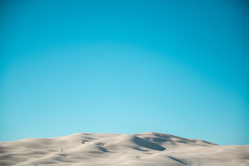 蓝天下的沙漠沙丘沙海上站着几个人