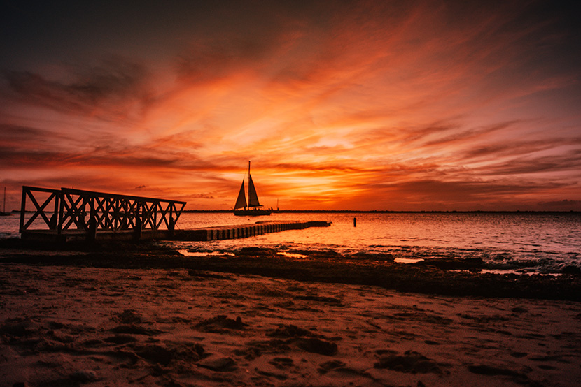 夕阳朝霞下的海边沙滩帆船