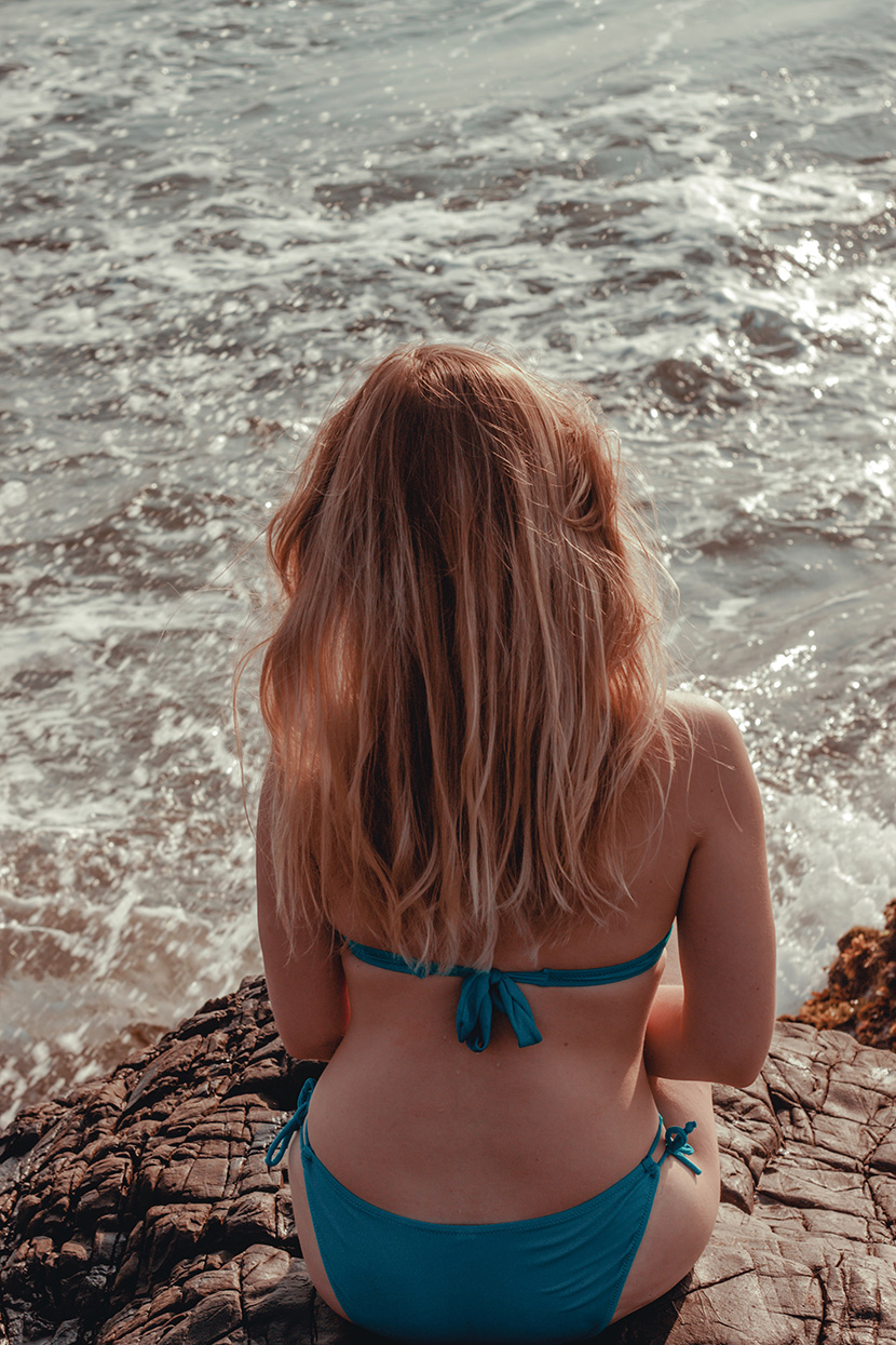 坐在海边礁石上的比基尼金发女人的性感背影