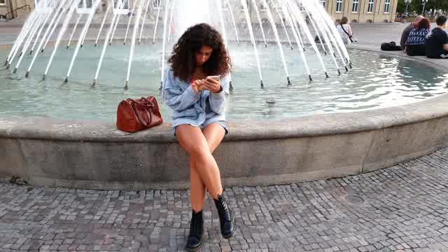 坐在喷泉边玩手机的女人短视频素材